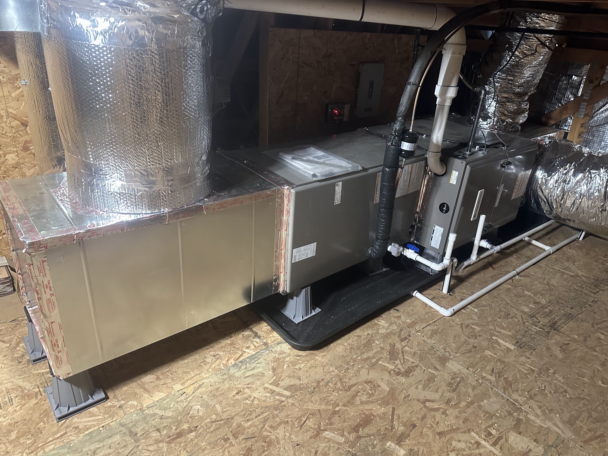 New air handler and furnace section installed on risers and a condensate pan in an attic, with new sheet metal plenum and insulated flex duct runs